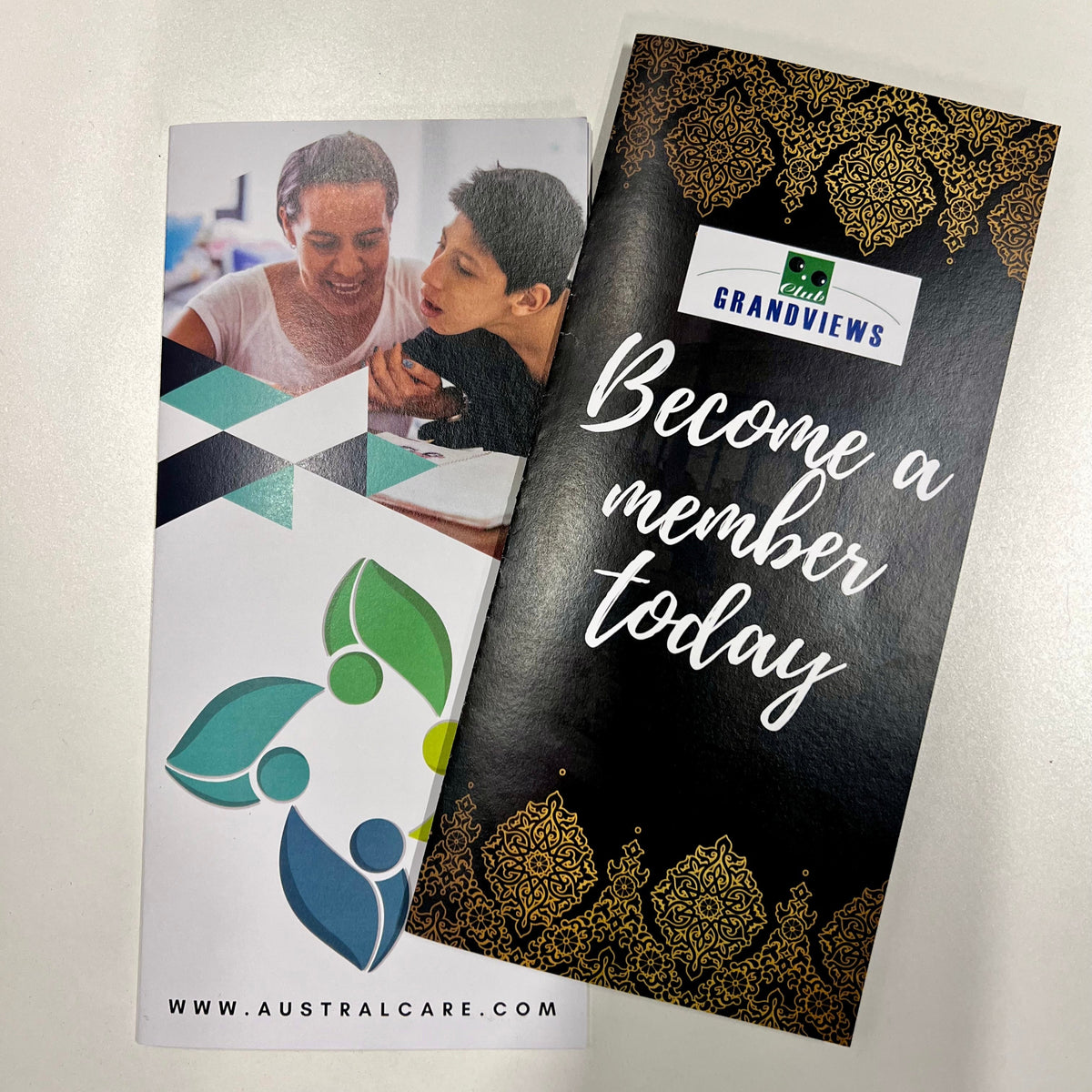 Two brochures on a white surface, one with a photo of two people and the other with text and branding.